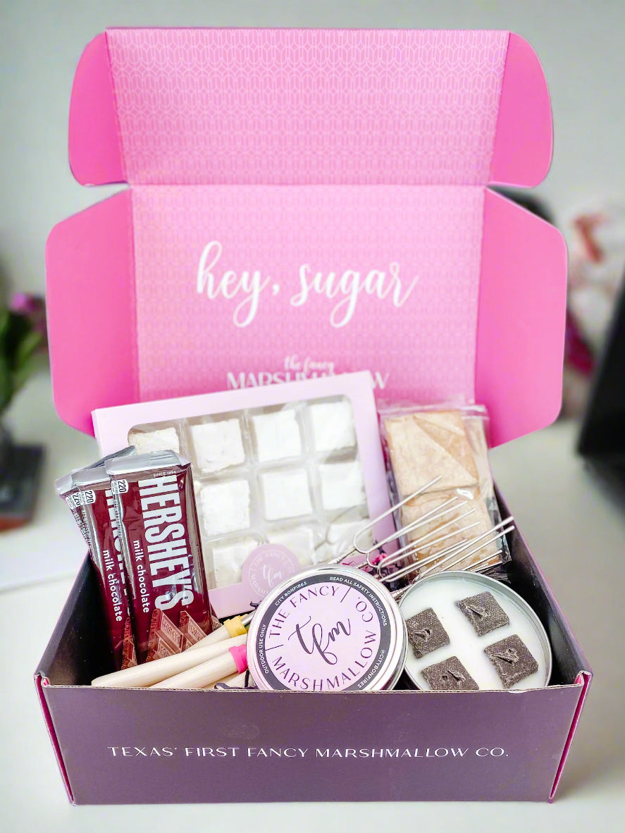 A pink box labeled 'hey, sugar' from Texas Frost Fancy Marshmallow Co. opened to display an assortment of marshmallows and other treats.
