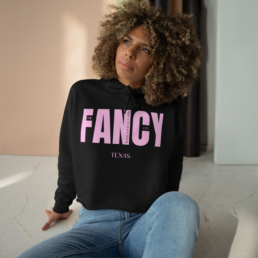 Woman wearing a black cropped hoodie with a large pink FANCY word over it shown.  